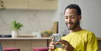 Jovem sorridente usando um smartphone.   Foto: Getty Images