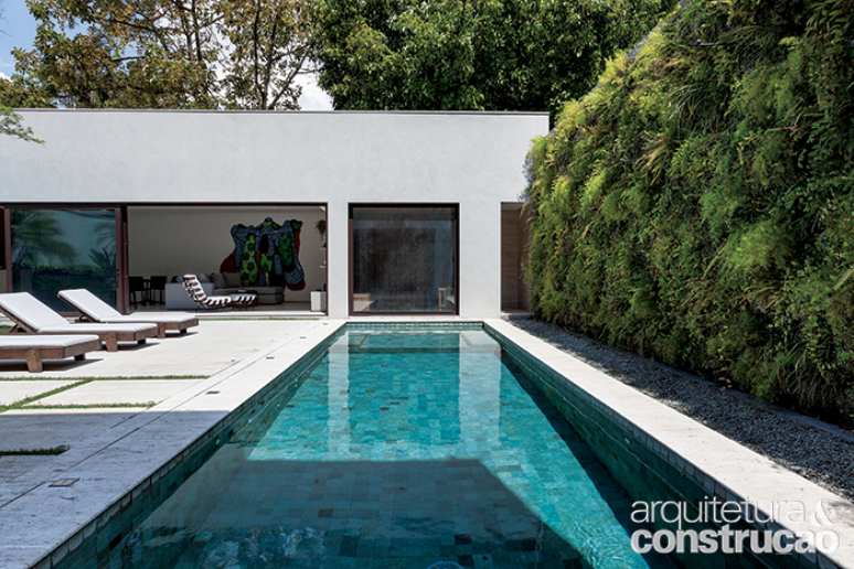 A piscina de 3 x 10,20 m é revestida de placas de 10 x 10 cm de pedra hijau lisa e tem bordas de travertino (materiais fornecidos pela Palimanan). A parede (à dir.) conquistou um jardim vertical com espécies de folhagens resistentes a fim de não sujar a piscina. Entre elas, estão aspargo, renda-portuguesa, hera e ripsális.